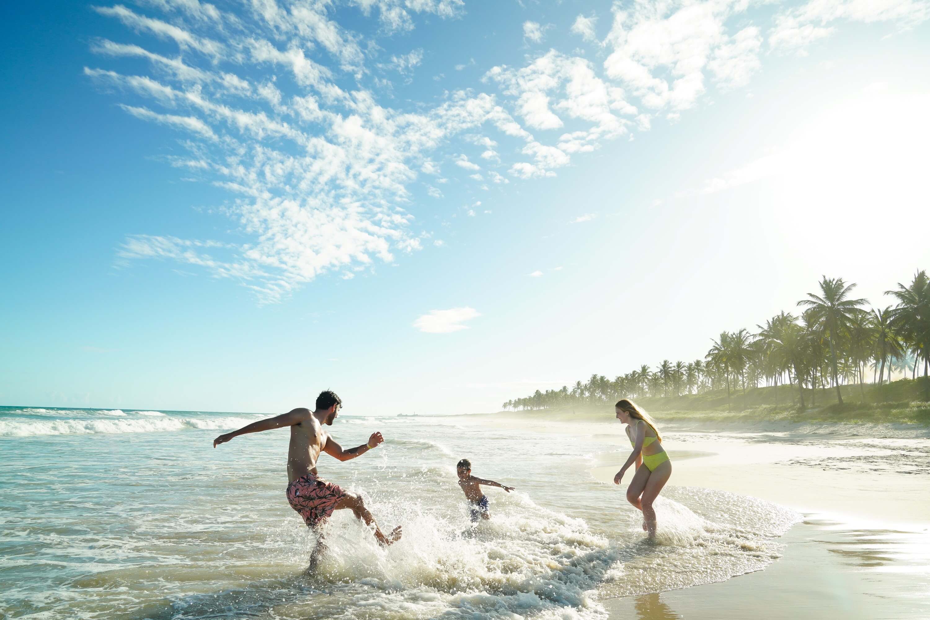 Família feliz brincando no mar da praia do Francês.